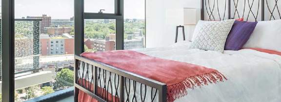 A bed with a red blanket and white pillows in a room with a view of the city.