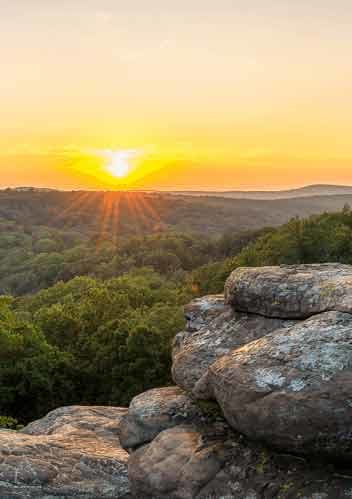 the sun setting over the mountains and trees in the forest