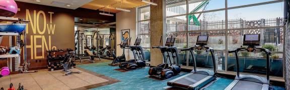 a gym with cardio machines and a pool in the background
