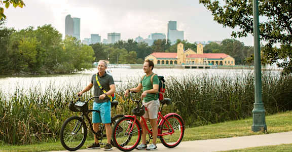 two men with bikes in front of a lake and a city skyline