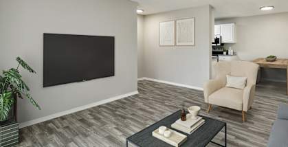 Model Living Room with Wood-Style Flooring and View of Kitchen at Arbors at Orange Park Apartments located in Orange, Park FL-HERO.