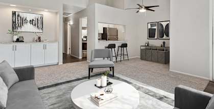 Model Living Room with Carpet and View of Kitchen at Verona Park Apartments located in Mesa, AZ-HERO.