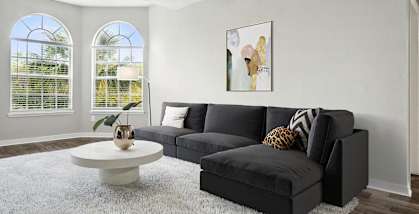 Model living room with a black couch and a white rug at The Vinings at Hunter's Green Apartments in Tampa, Florida