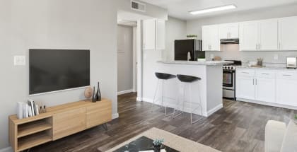 Model apartment kitchen and living room with white cabinets and a television