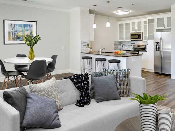 A modern living room with a grey couch and a kitchen in the background. at Apex Mission Valley, California, 92108