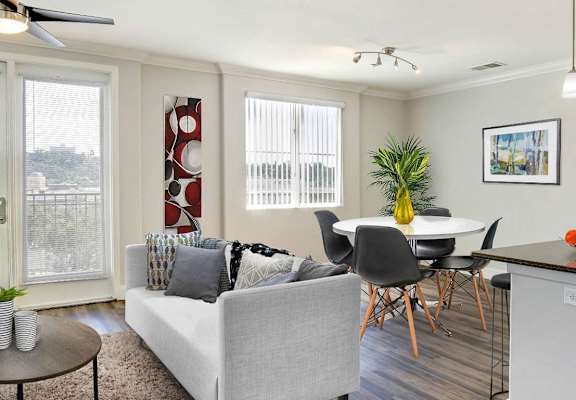 A living room with a grey couch and a dining table with chairs. at Apex Mission Valley, San Diego, CA