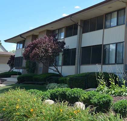 A building with a brown and beige exterior and a small garden in front.