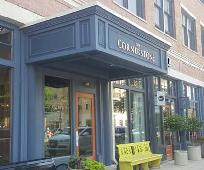 A storefront with a blue awning and a yellow bench outside. at Cornerstone & Ravenna* Apartments, Shorewood, Wisconsin