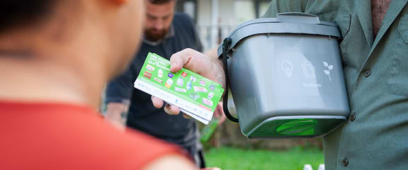 a man is holding a recycling bin and a woman is looking at a recycling container