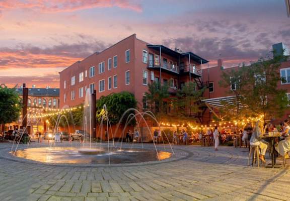 a fountain in a plaza with people sitting at tables and chairs and a building in the background  at Iron Works Sono, Norwalk, Connecticut