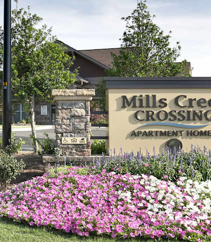 the front of mills creek crossing apartments sign with flowers in front of the building