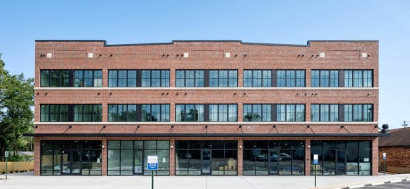 A large red brick building with a flat roof and a blue sign on the ground. at The Mobile Lofts, Alabama