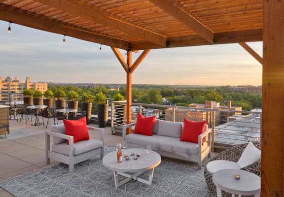 A wooden pergola over a patio with white furniture and a view of the city.