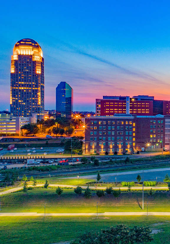 A city skyline at dusk with a prominent building featuring a large dome-like structure.