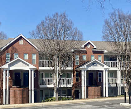 A red brick building with white columns and a black fence.