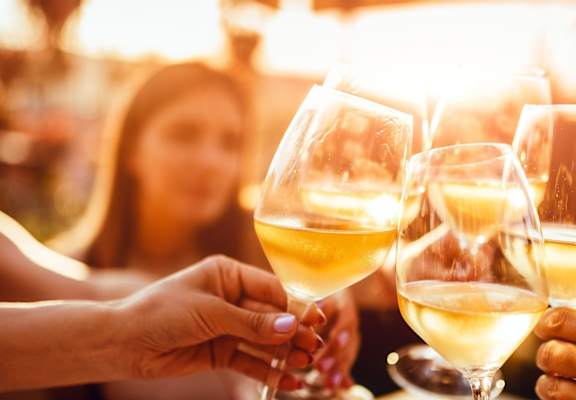 A group of people toasting with glasses of white wine.