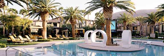 A pool surrounded by palm trees and lounge chairs.