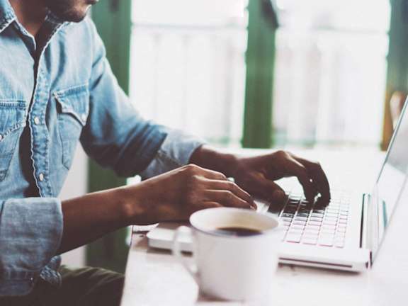 Man Working on Laptop with Cup of Coffee Next to Him