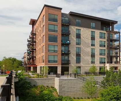 The view of two beige, tan, and brown apartment buildings surrounded by trees at Inspire Apartments. 