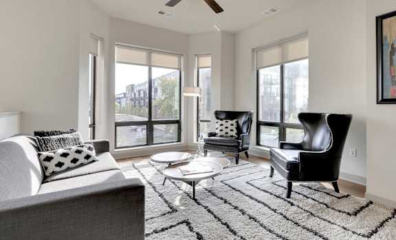 The living room with a couch, plush chairs, coffee table, decorations, and window at Inspire Apartments. 