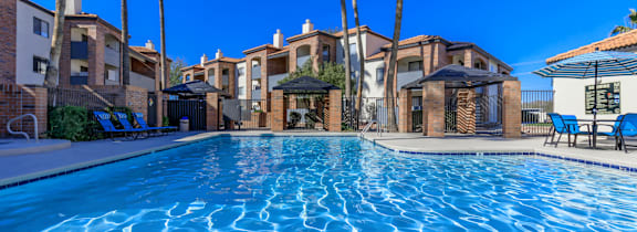 A swimming pool in front of a resort with a sun lounger.