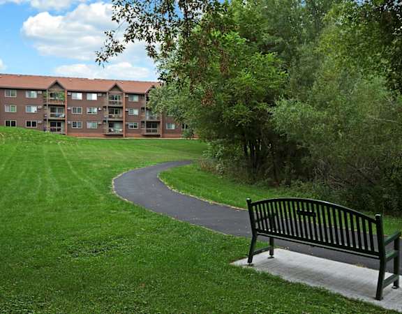 a park bench sitting next to a path in the grass  at Park Pointe, St. Louis Park, MN