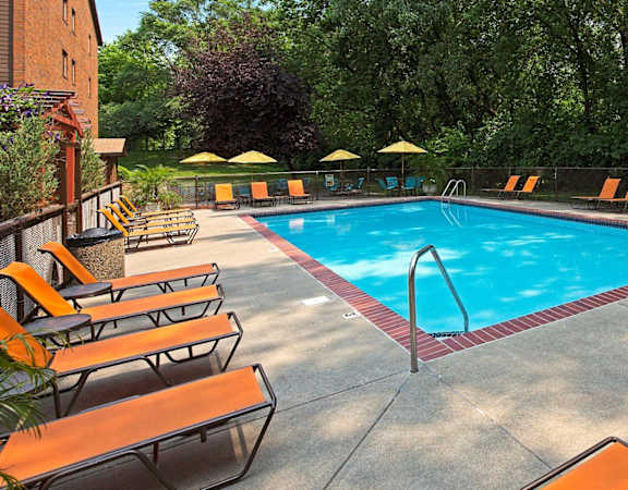 A pool surrounded by orange lounge chairs and umbrellas. at The Gables at Park Pointe, St. Louis Park, 55426