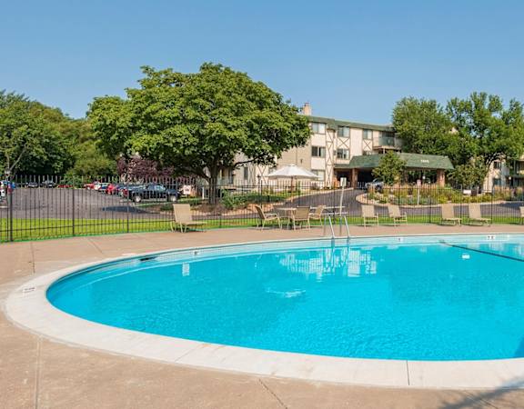 A large outdoor swimming pool surrounded by trees and a fence. at Medicine Lake Apartments, Plymouth, MN, 55441