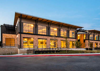 A modern building with a combination of brick and glass facade is illuminated during the evening.
