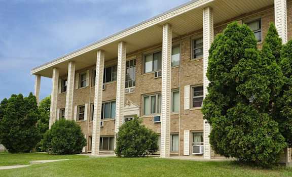 a large brick apartment building with columns and green grass
