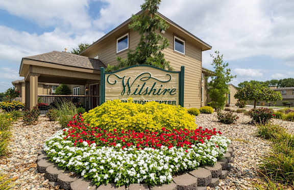 Exterior view of the Wilshire clubhouse, featuring a large building with a welcoming entrance, wide windows, and surrounding landscaping,