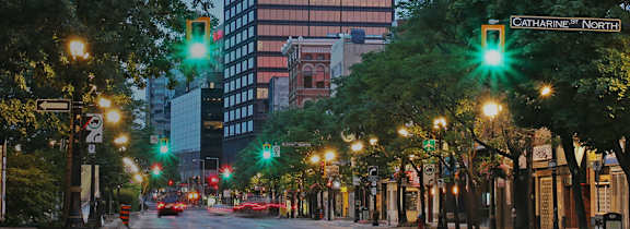 A black car is driving down a street with people walking on the sidewalk.