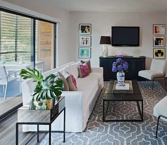 A living room with a white couch, a coffee table, and a television on the wall.