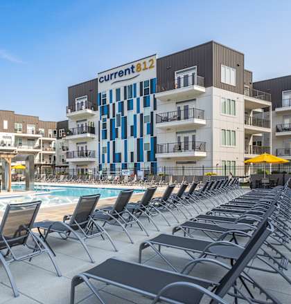 A pool area with chairs and a building with a sign that says "Current 812".