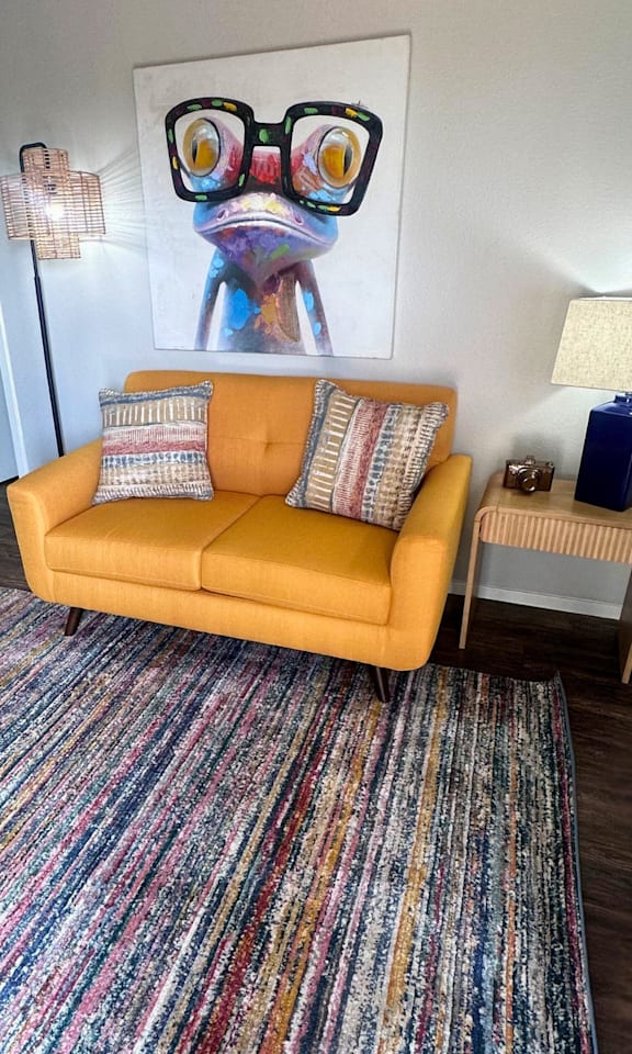 A living room with a yellow couch and a colorful rug.