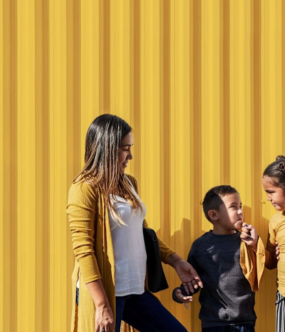 A woman and two children are standing in front of a yellow striped wall.