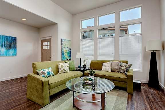 A living room with a green couch and a glass coffee table at Verraso Village Townhomes in Meridian, 83646