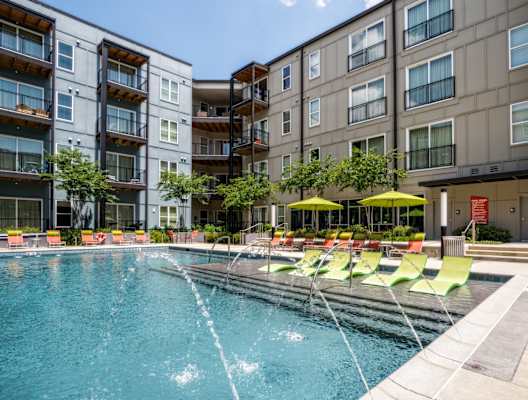 a swimming pool with yellow and green chairs in front of an apartment building