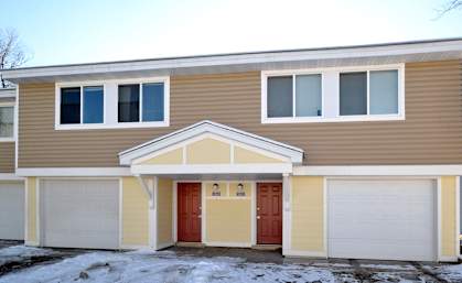 A two-story house with a red door and white garage doors.