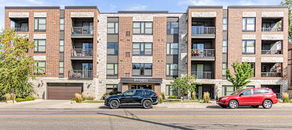 A black car is parked in front of a red car in front of a brick building.