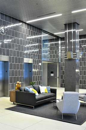 A modern living room with a grey couch, a grey chair and a black and white tiled wall.