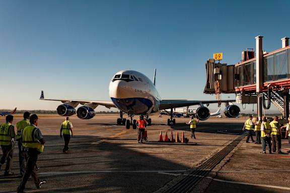 A large airplane is parked on the tarmac with several people in high visibility vests walking around it.