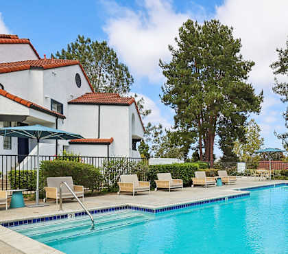 A swimming pool in front of a white building with a red tile roof.