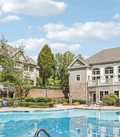 A swimming pool in front of a house with a brick wall.
