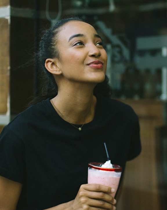 A woman in a black shirt is holding a cup with a straw in it.