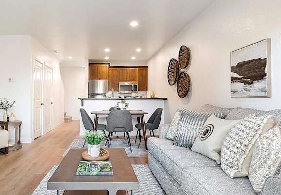 A modern living room with a grey sofa, wooden dining table, and a white chair.