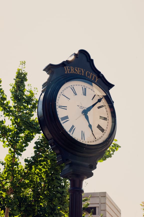 a large clock on a pole next to a tree at 100 House Apartments, Jersey City , New Jersey