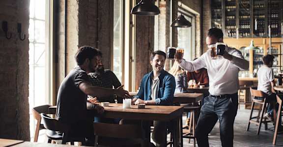 A man is serving drinks to two men seated at a table in a restaurant.