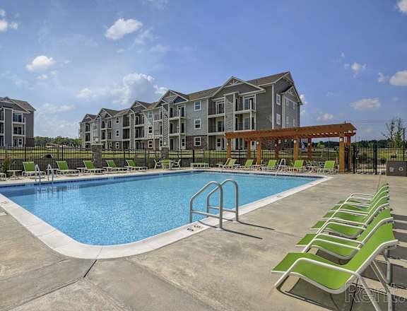 a swimming pool with green chairs and an apartment building in the background at Dodson Pointe Apartment Homes, Rogers, AR, 72758