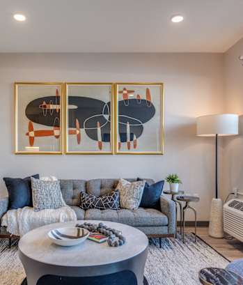 A living room with a grey couch, a brown chair, a coffee table, and a painting on the wall.